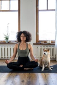 Black woman sits in a yoga or meditation pose with a shiba inu dog sitting next to her.